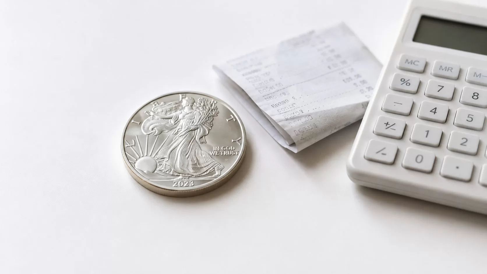 A 2023 silver coin sitting on a table next to a paper receipt and a white calculator.